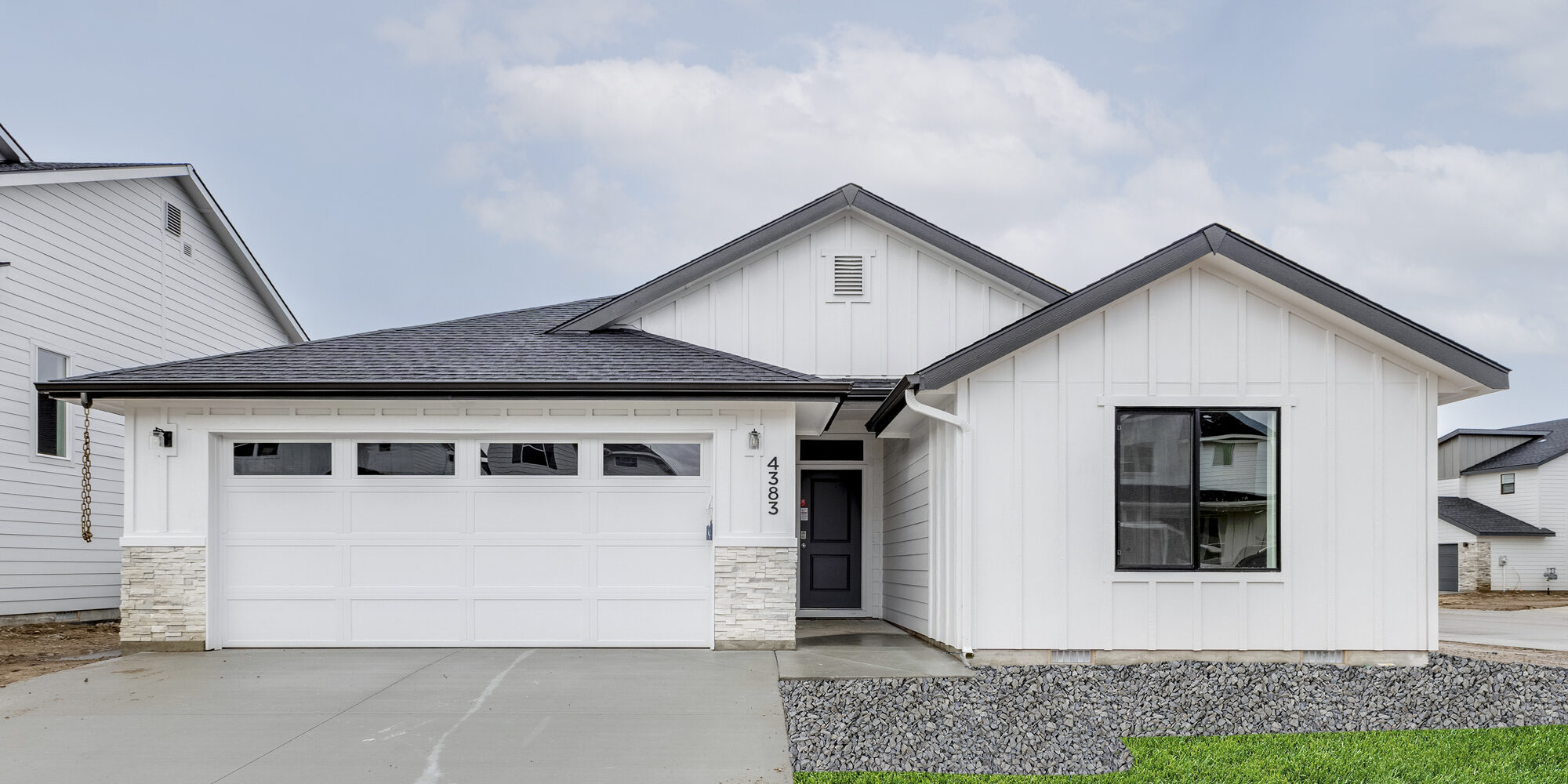 A modern white farmhouse-style home with a black roof, large front window, and two-car garage, set in a developing neighborhood. This home is an example of homes that are part of the upcoming Deer Valley community by CBH Homes, offering brand-new homes in a sought-after location. Stay tuned for more details on availability and home designs coming soon!